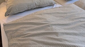 Ein ordentlich bezogenes Bett mit gestreifter Bettwäsche, ein Kopfteil mit gerahmtem Kunstwerk und eine Nachttischlampe.