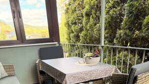 Ein Balkon mit Korbmöbeln, einem Tisch mit gemustertem Tischlauf und Blick ins Grüne.