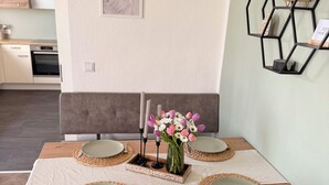 Ein Essbereich mit Holztisch, gedeckten Plätzen für vier Personen, grauen Stühlen, einer Blumenvase und einem sechseckigen Regal mit einem gewebten Korb.
