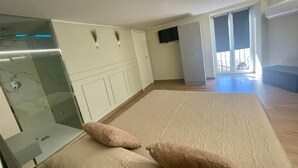Ein geräumiges Zimmer mit einem großen Bett, einer Duschkabine aus Glas, einem Fernseher und einem Balkon mit Aussicht.