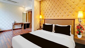 A hotel room with a large bed, a bedside table, a desk, a mirror, and a wall with a tufted headboard.
