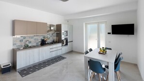 Une cuisine moderne avec un coin repas, un téléviseur fixé au mur et une fenêtre laissant entrer la lumière naturelle.