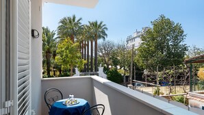 Un balcon avec une table et des chaises, une vue sur des palmiers et des immeubles, et une balustrade blanche.