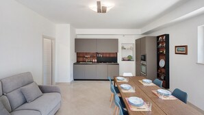 A modern living room with a sofa, a dining table set for four, and a kitchen in the background. - Villa Cappuccini – Lower Floor Apartment with Shared Terrace, Wi-Fi & Air Conditioning (Sant'Agnello)