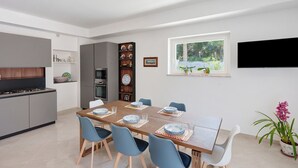 A modern kitchen with grey cabinets, a built-in oven, and a dining area with a wooden table and blue chairs. - Villa Cappuccini – Lower Floor Apartment with Shared Terrace, Wi-Fi & Air Conditioning (Sant'Agnello)