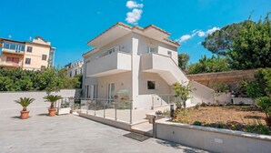 Un edifici residencial de diversos pisos amb teulada plana, un balcó i una zona de jardí.