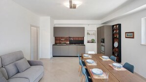Un saló modern amb un sofà, una taula de dinar preparada per a quatre persones i una cuina al fons.