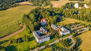 Luchtbeeld van een groot landgoed met meerdere gebouwen, waaronder een hoofdgebouw en diverse kleinere constructies, omgeven door uitgestrekte groene velden en beboste gebieden.