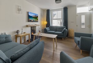 Ein Wohnzimmer mit einer Couch, einem Tisch, einem Kamin und einem Fernseher.