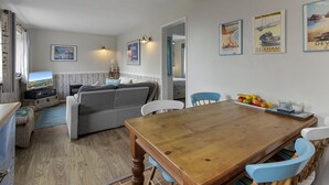 A cozy living room with a wooden dining table, a sofa, and a kitchen area with a view. - No.1 Cottage is a charming and cosy South Devon holiday cottage (Brixham)