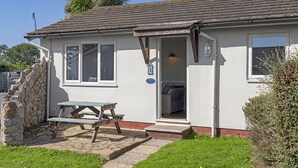 A white building with a stone wall, a wooden bench, and a door leading inside. - No.1 Cottage is a charming and cosy South Devon holiday cottage (Brixham)
