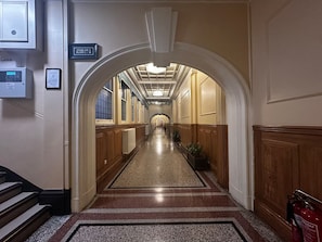 Ein Hotelgang mit einem zentralen Teppichläufer, Holzvertäfelung an den Wänden und einem Schild, das den Standort der Treppe angibt.