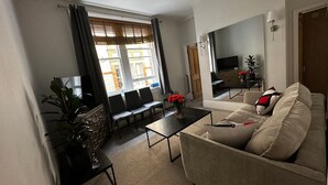 A living room with a sofa, coffee table, TV, and a dining area with chairs and a table. - Luxury Living at Charing Cross 26 | Best of London (London)