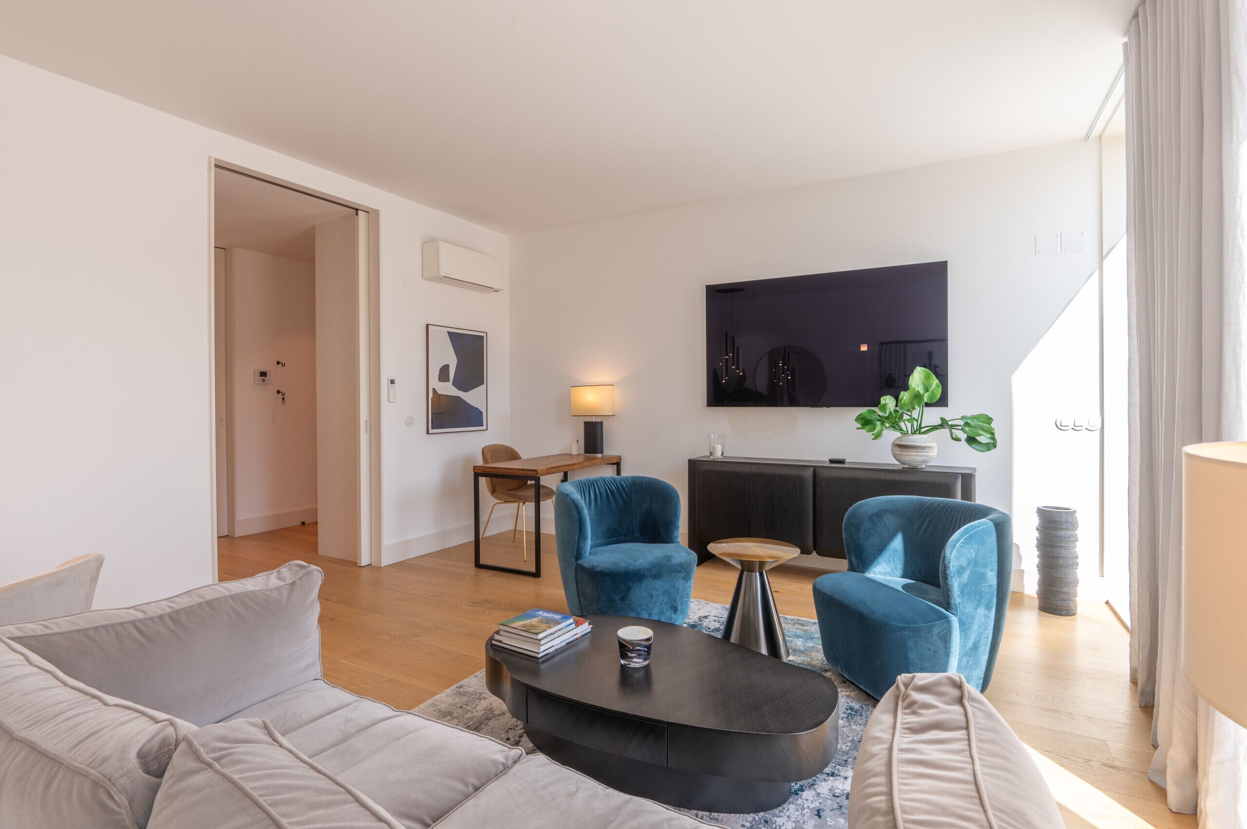 Un salon moderne avec un canapé, deux fauteuils bleus, une table basse, un téléviseur et une plante en pot.