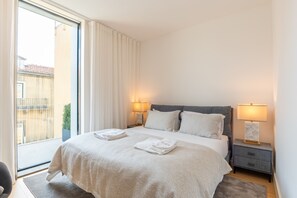 A hotel room with a bed, two bedside lamps, a nightstand, a window with curtains, and a view of the outside. - FLH Liberdade Balcony Apartment II (Lisboa ciudad)