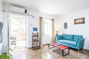 Ein Wohnzimmer mit einem blauen Sofa, einem farbenfrohen Couchtisch, einer Holzleiter und einer Tür, die auf einen Balkon führt.