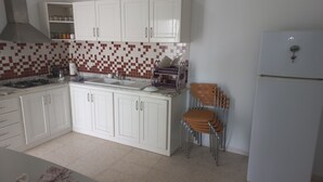 Una cocina con armarios blancos, salpicadero de azulejos, un lavabo, una estufa y una silla.