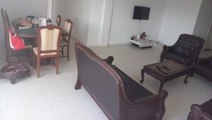Una sala de estar con una mesa de comedor, sillas, un sofá, un televisor y una mesita con objetos encima.