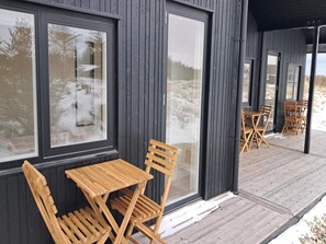 Eine Holzterrasse mit Sitzgelegenheiten im Freien und großen Fenstern.