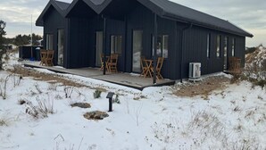 A modern, dark-colored building with multiple rooms, a covered outdoor area with chairs, and a snow-covered landscape. - 4 Star Holiday Home in Lokken (Lokken)