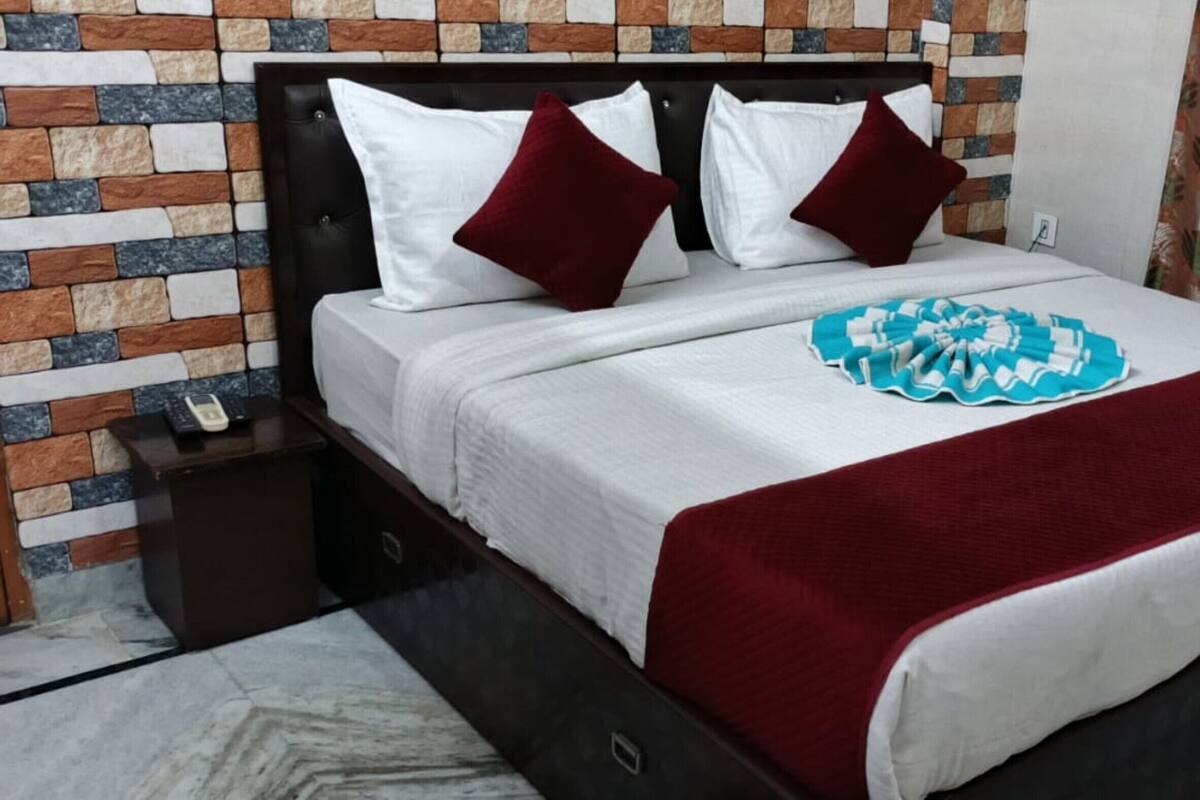 Cama com colcha vermelha e branca, duas almofadas brancas e um objeto decorativo azul.