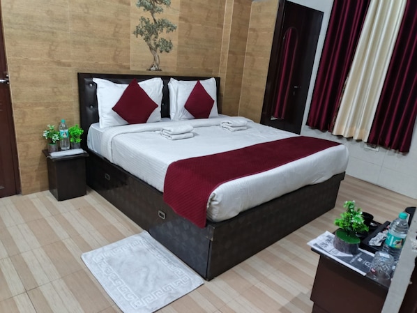 Quarto de hotel bem arrumado, com uma cama, mesa de cabeceira, uma pequena mesa com uma planta e uma janela com cortinas.