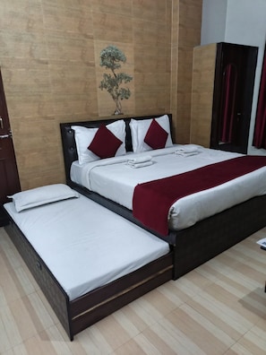 Uma cama de casal com cabeceira escura, roupa de cama branca e almofadas vermelhas.