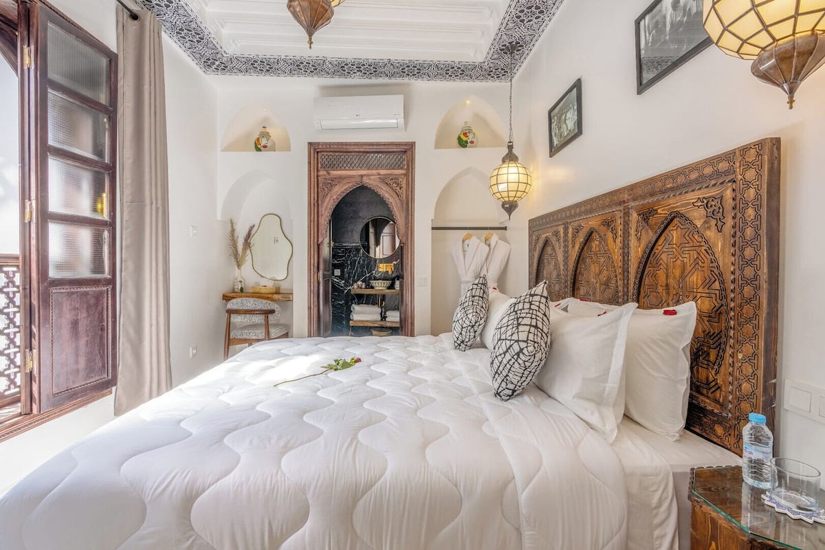 A hotel room with a large bed, a wooden headboard, a mirror, and a view of a bathroom.