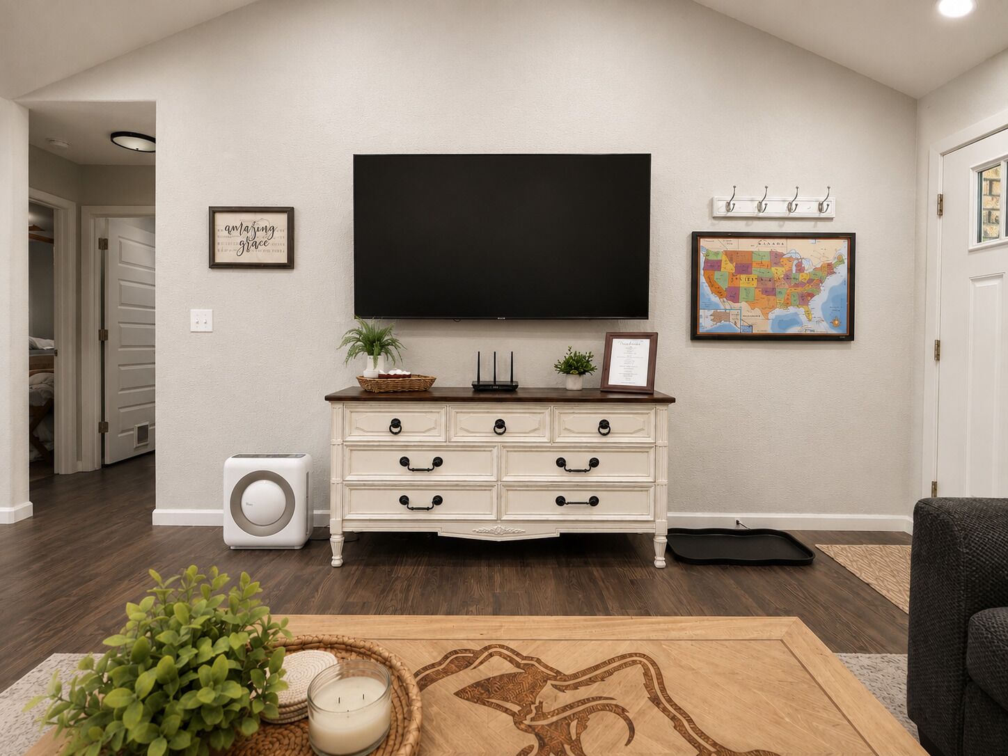 A living room with a flat-screen TV, a white dresser, a map on the wall, and a plant on the dresser.
