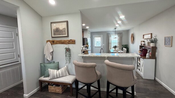 A modern kitchen with a central island, a dining area with two chairs, a bench, and a small table. - Peaceful 4-bedroom Fayetteville getaway near the University of Arkansas! Enjoy a heated & cooled game room, fenced backyard with playground, gas grill, and plenty of space for the whole family. (Fayetteville)