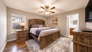 A bedroom with a wooden bed, a ceiling fan, a window with blinds, a nightstand, a dresser, and a TV mounted on the wall. - Peaceful 4-bedroom Fayetteville getaway near the University of Arkansas! Enjoy a heated & cooled game room, fenced backyard with playground, gas grill, and plenty of space for the whole family. (Fayetteville)