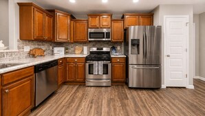 A kitchen with wooden cabinets, stainless steel appliances, a microwave, oven, and refrigerator. - Peaceful 4-bedroom Fayetteville getaway near the University of Arkansas! Enjoy a heated & cooled game room, fenced backyard with playground, gas grill, and plenty of space for the whole family. (Fayetteville)