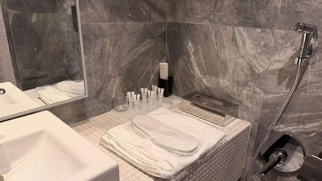Un baño con lavamanos blanco, espejo, toallero y zona de ducha.