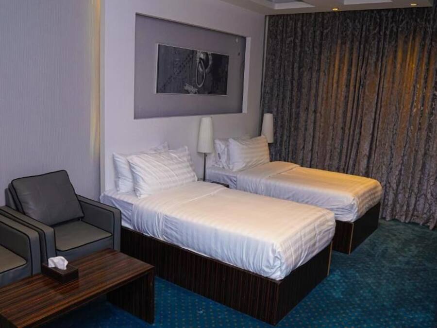 A hotel room with two beds, a sofa, a small table, a painting on the wall, and a curtain.
