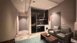 Un espacio habitable compacto con kitchenette, un sofá, una mesa de centro y un televisor.