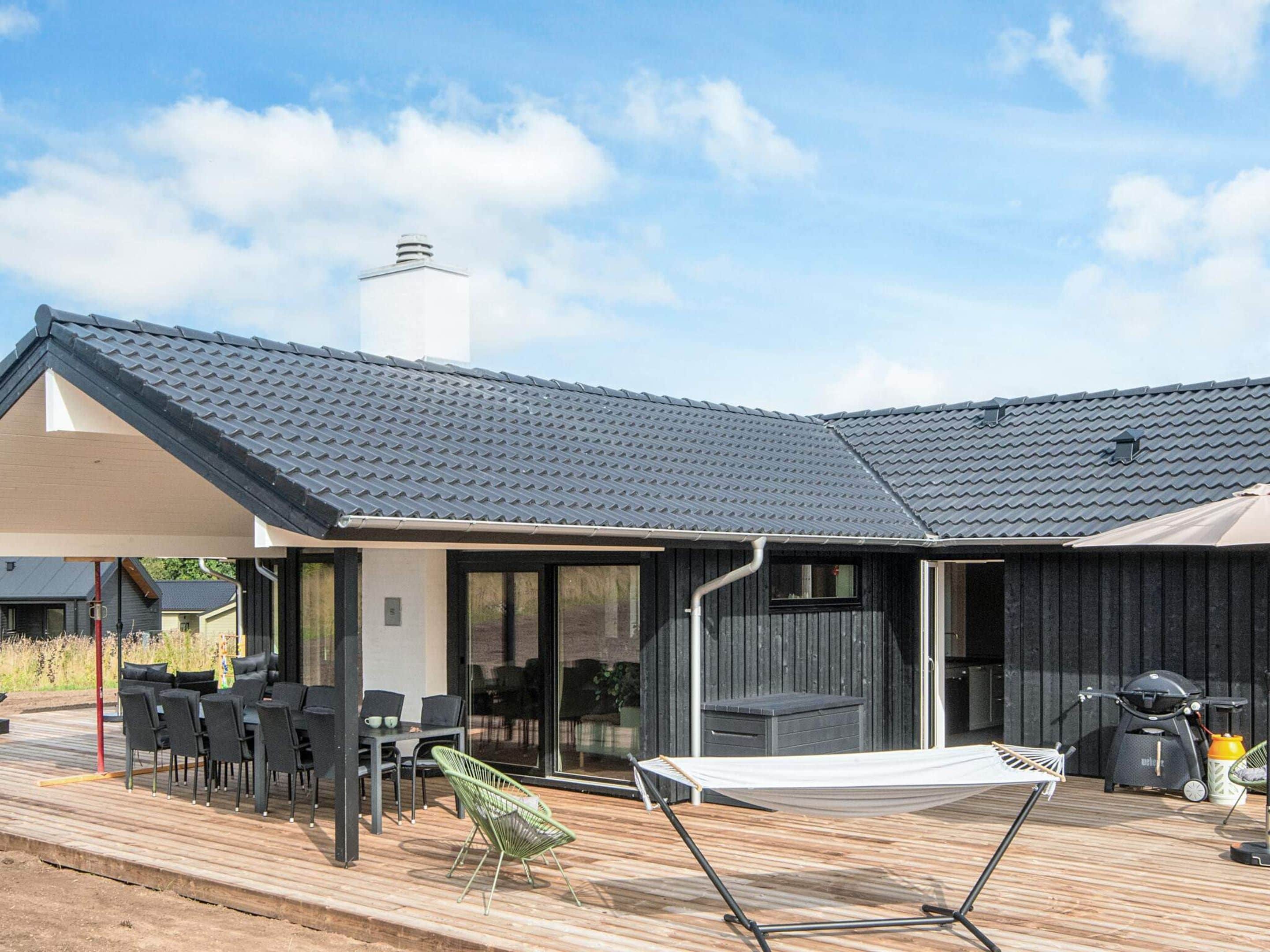 Een modern huis met een overdekt terras, buitenmeubels en een barbecueplek.