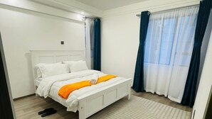 Quarto com cama, luminária no teto, janela com cortinas e tapete com padrão herringbone.