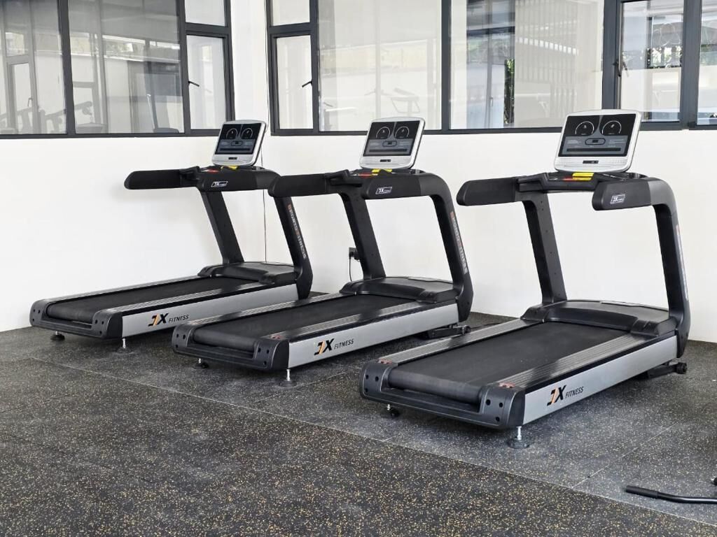 Three treadmills with digital displays in a room with large windows.