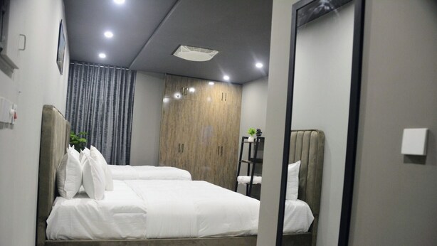 Une chambre à coucher moderne avec un lit, une armoire, un miroir et une étagère ornée d’une plante.