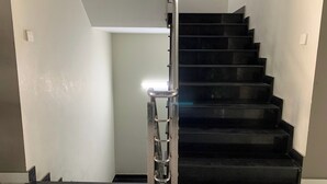 Un escalier moderne avec des marches noires et une rampe métallique, menant à un palier où se trouve un luminaire.