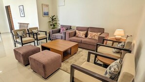 Ein modernes Wohnzimmer mit einer Sofagarnitur, Sesseln, Poufs, einem Couchtisch und einer Lampe.