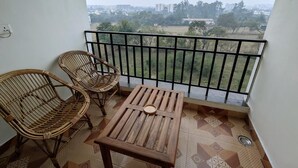 Ein Balkon mit Tisch und zwei Korbstühlen, einem Metallgeländer und Blick auf eine Stadtlandschaft.