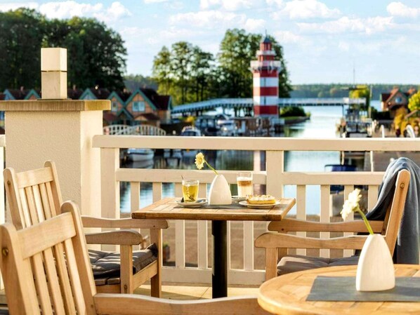 A wooden deck with a table and chairs, overlooking a water body with boats and a lighthouse. - 4 Person Holiday Park Home in Grosszerlang (Rheinsberg)