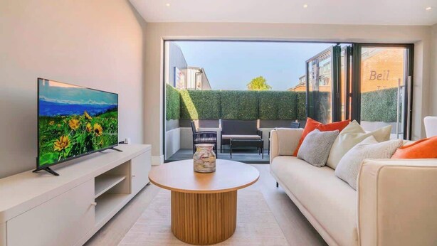 Ein modernes Wohnzimmer mit Flachbildfernseher, rundem Holztisch, Sofa und einer Schiebeglastür zu einem Außenbereich.