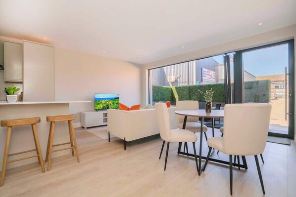 A modern kitchen with a TV, white furniture, and a large window. - Wimbledon 2BR | Indoor-Outdoor Living & Patio (London)