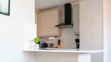 A modern kitchen with white cabinetry, a black range hood, and two wooden stools.