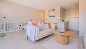 A modern living room with a sofa, a coffee table, and a kitchen area in the background. - Wimbledon 2-Bed | Private Patio | Sleeps 4 (London)