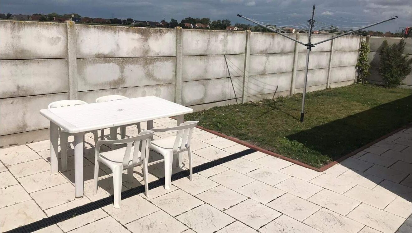 Eine Terrasse mit weißem Tisch und Stühlen, einer Betonmauer und einem Rasenstück.