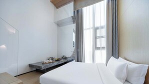 Une chambre d’hôtel moderne dotée d’un grand lit, d’une table de chevet, d’une banquette intégrée et d’une grande fenêtre avec des rideaux.