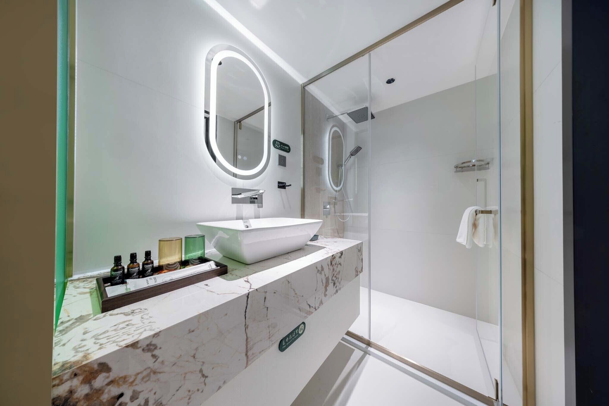 Un bagno moderno con un mobile vanitario in marmo, un ampio specchio con illuminazione integrata, un box doccia in vetro e un portasciugamani a vista.